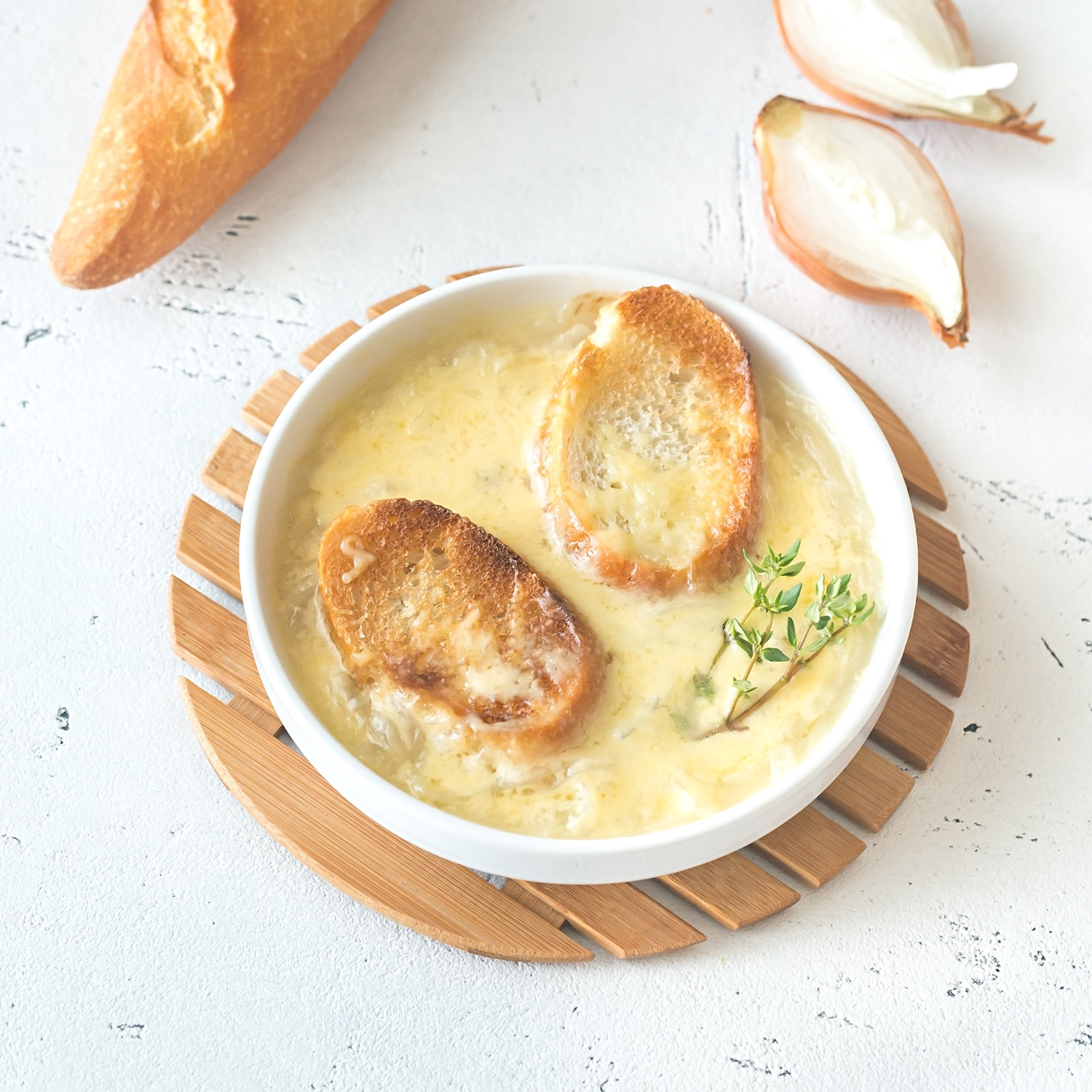 Crema de cebolla y ajo en una tazón hondo acompañada de pan. Alrededor hay pan y ajos. Todo sobre un fondo claro.