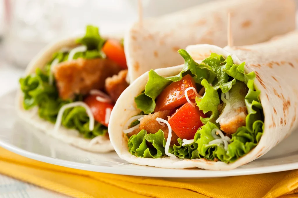 Vista dde dos wraps de pollo con lechuga y trozos de tomate sobre un plato blanco