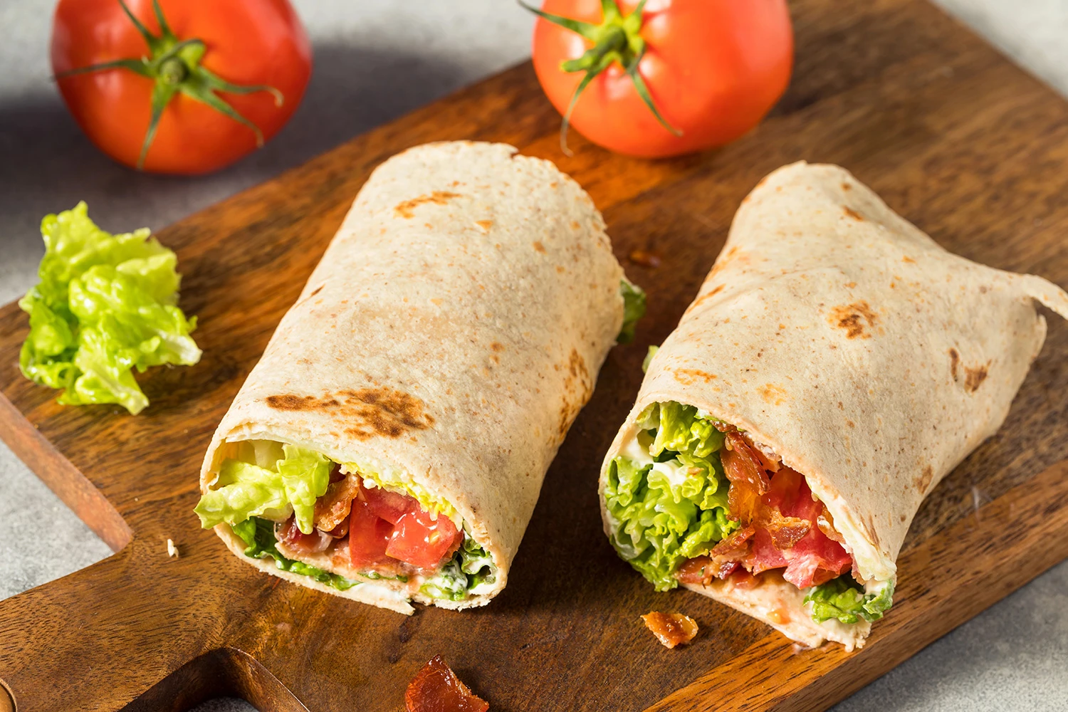 Vista de dos wraps de pollo con lechuga y trozos de tomate sobre una tabla de madera oscura