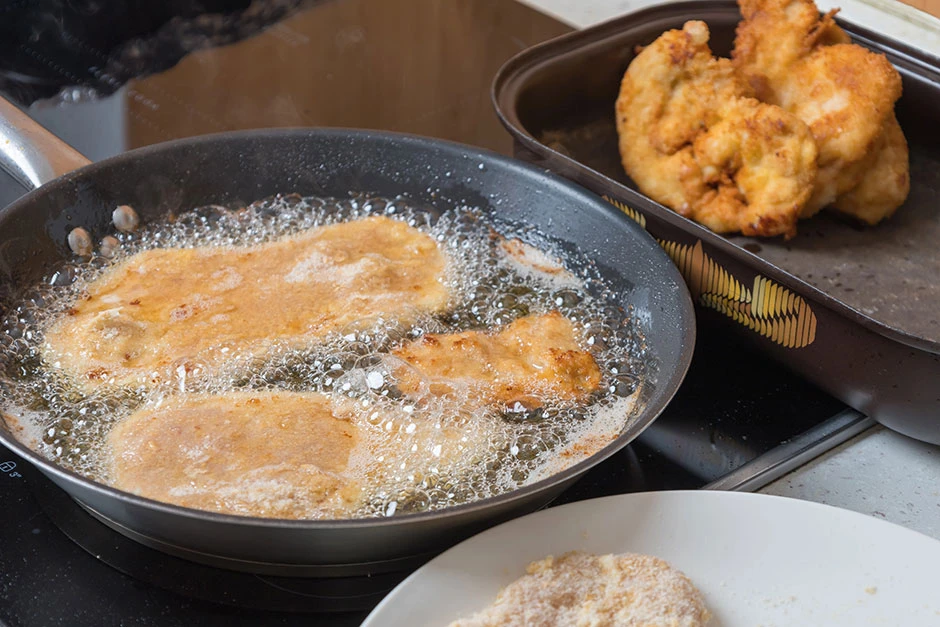 Alimentos apanados cocinándose en una sartén con aceite caliente, mostrando el proceso de fritura sobre una estufa.