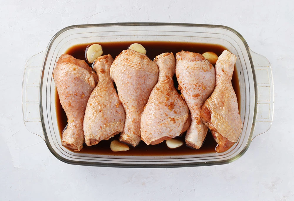 Piezas de pollo crudo marinadas con especias y ajo, organizadas en una refractaria de vidrio antes de llevar al horno.